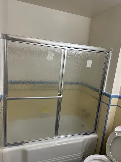 Framed sliding textured-glass bath screen and towel bar above a bathtub.